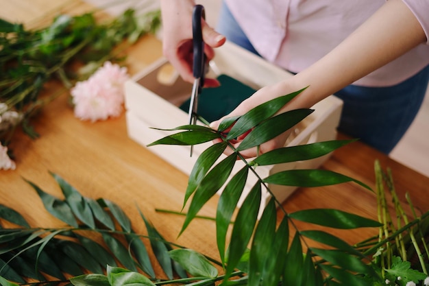 Floreria en el trabajo manos de mujer joven haciendo composición moderna de moda de diferentes flores en casa