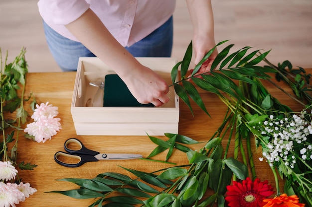 Floreria en el trabajo manos de mujer joven haciendo composición moderna de moda de diferentes flores en casa