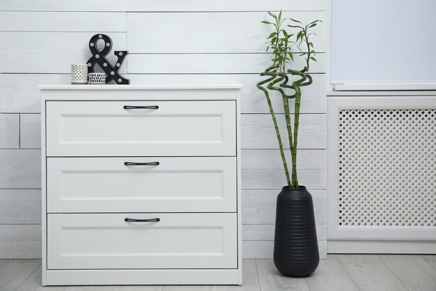 Foto florero con bambú de la suerte en el piso cerca de la cómoda en la habitación interior elegante