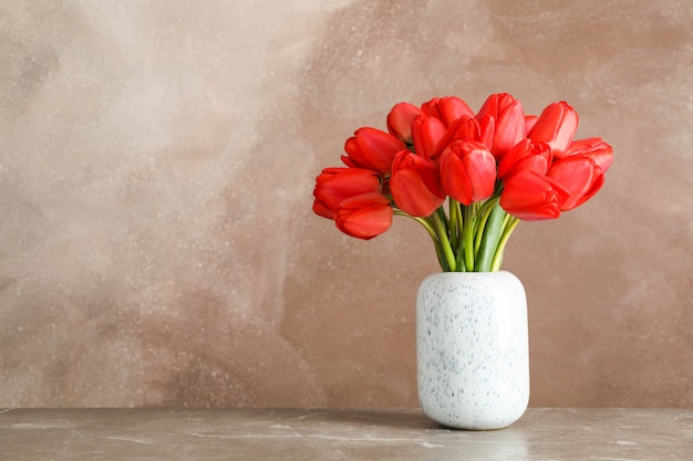 Florero con hermosos tulipanes rojos en la mesa contra marrón