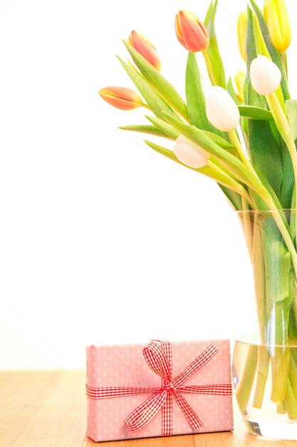 Florero de tulipanes en la mesa de madera con regalo