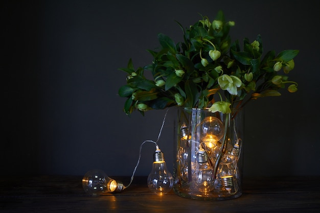 Florero de vidrio lleno de bombillas luminosas y un ramo de hellebore