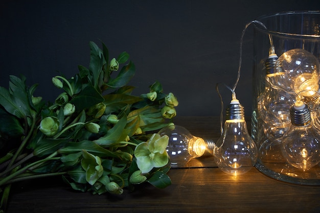 Florero de vidrio lleno de bombillas luminosas y un ramo de hellebore