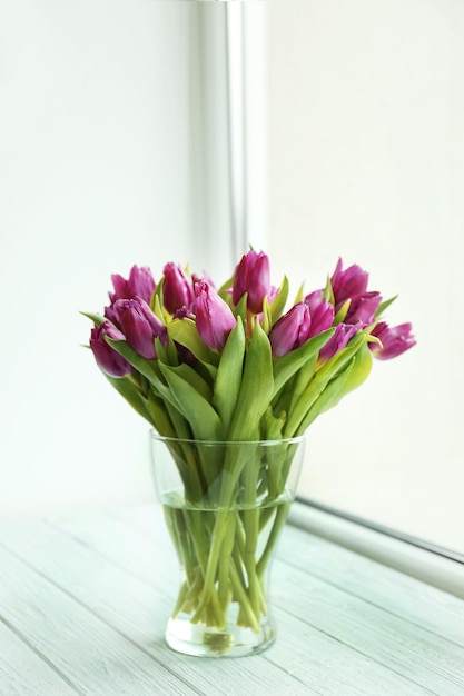 Florero de vidrio con ramo de hermosos tulipanes en el alféizar de la ventana