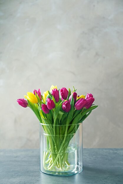 Florero de vidrio con ramo de hermosos tulipanes sobre fondo de color