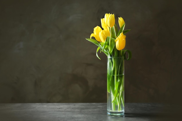 Florero de vidrio con ramo de hermosos tulipanes sobre fondo de color