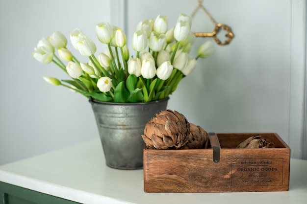 Flores de alcachofa en caja de madera y un ramo de tulipanes blancos en un jarrón