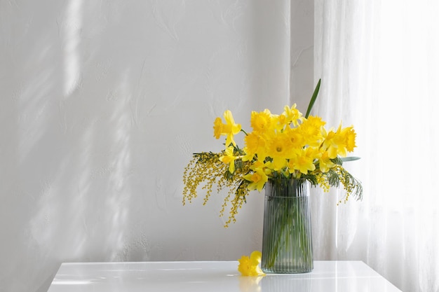 Flores amarelas da primavera em vaso de vidro no fundo branco