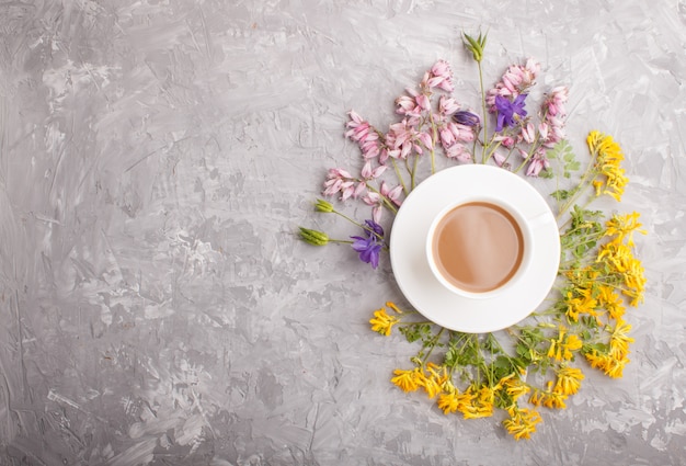 Flores amarelas, rosa e azuis em uma espiral e uma xícara de café em um concreto cinza