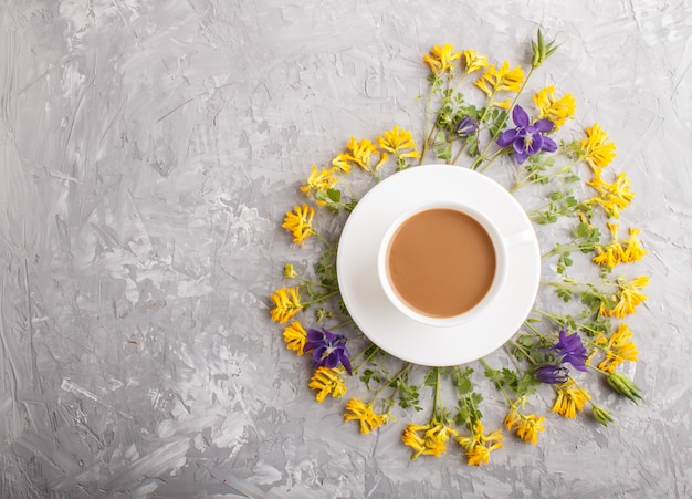 Flores amarillas y azules en una espiral y una taza de café en un concreto gris