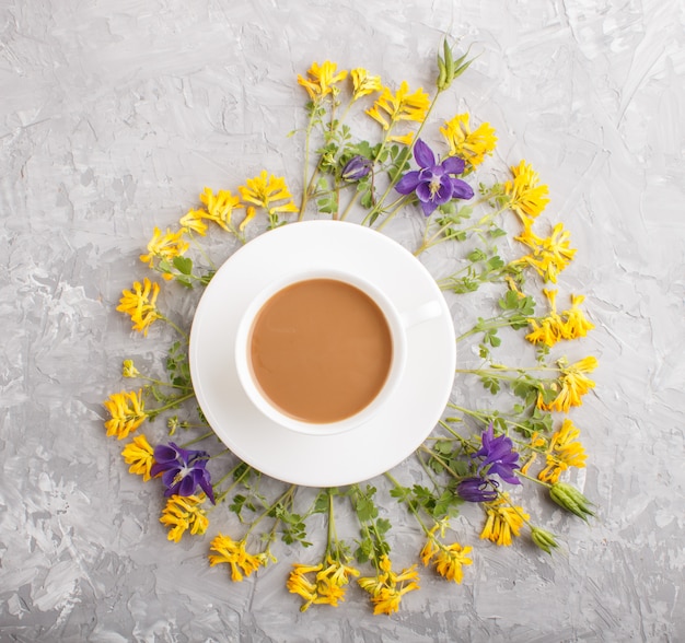 Flores amarillas y azules en espiral y una taza de café sobre un fondo de hormigón gris