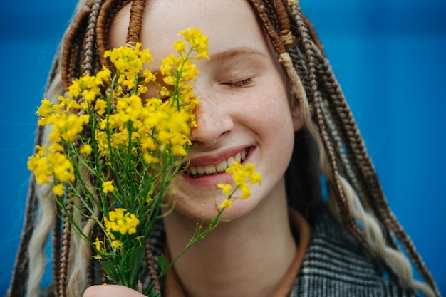 Flores amarillas en una mano frente a una cara de niña despreocupada con los ojos cerrados