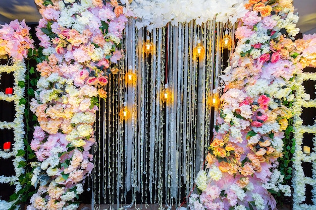 Flores artificiais coloridas com lâmpadas decorativas antigas estilo Edison penduradas na decoração do palco do casamento