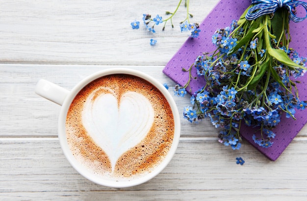 Flores azules nomeolvides, cuaderno y una taza de café caliente.