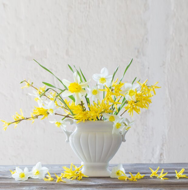 Flores brancas e amarelas da primavera em um vaso na superfície da velha parede branca