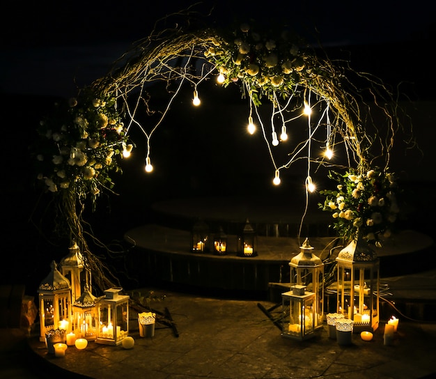 Foto flores brancas em arco na cerimônia de casamento. decoração ao ar livre. estilo rústico romântico. luzes de lâmpadas à noite.