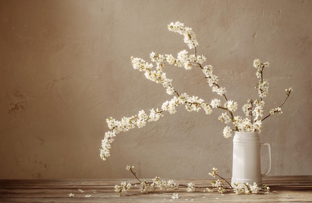 Flores de cerezo en jarra blanca sobre mesa de madera antigua