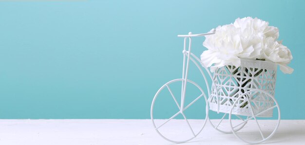 Flores de clavel blanco en una bicicleta blanca decorativa sobre un fondo azul Regalo floral para una boda o cumpleaños