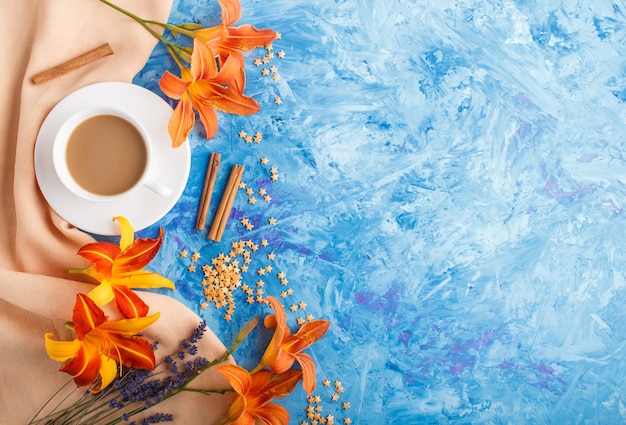 Flores de color naranja lirio y lavanda y una taza de café sobre un fondo de hormigón azul, con textil naranja. Morninig, primavera, composición de moda. Endecha plana, vista superior, espacio de copia.