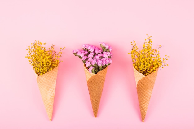 Flores cor-de-rosa e amarelas em cones do waffle para o gelado em um fundo brilhante. vista superior, lay plana