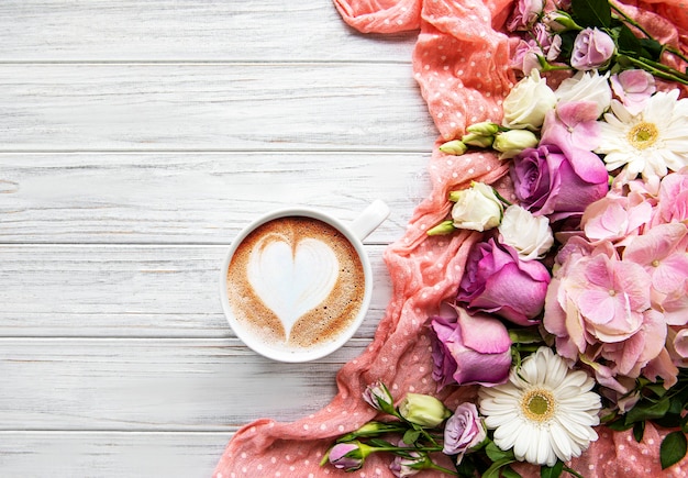 Flores cor de rosa e uma xícara de café em um fundo branco de madeira