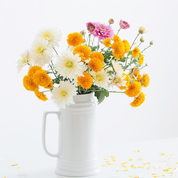 Flores de crisantemo en jarra blanca sobre fondo de pared blanca