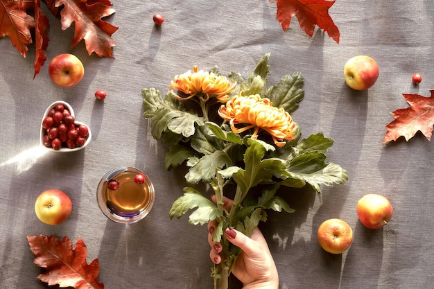 Flores de crisantemo de otoño amarillas y naranjas en la mano Calabazas manzanas arándano y hojas de roble rojo Decoraciones de otoño vista superior plana