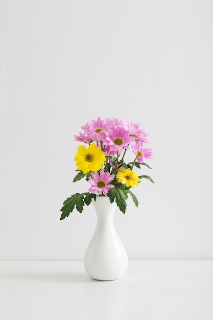 Flores de crisantemos en jarrón de cerámica sobre fondo blanco.