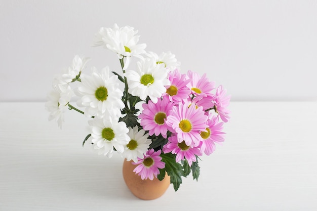 Flores de crisantemos en jarrón de cerámica sobre fondo blanco.