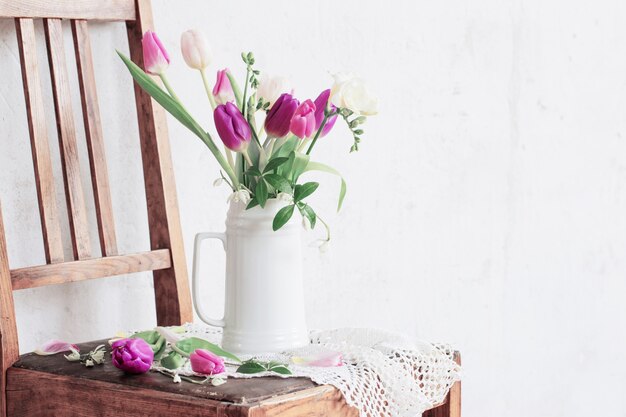 Flores da primavera em uma cadeira velha na velha parede branca de fundo