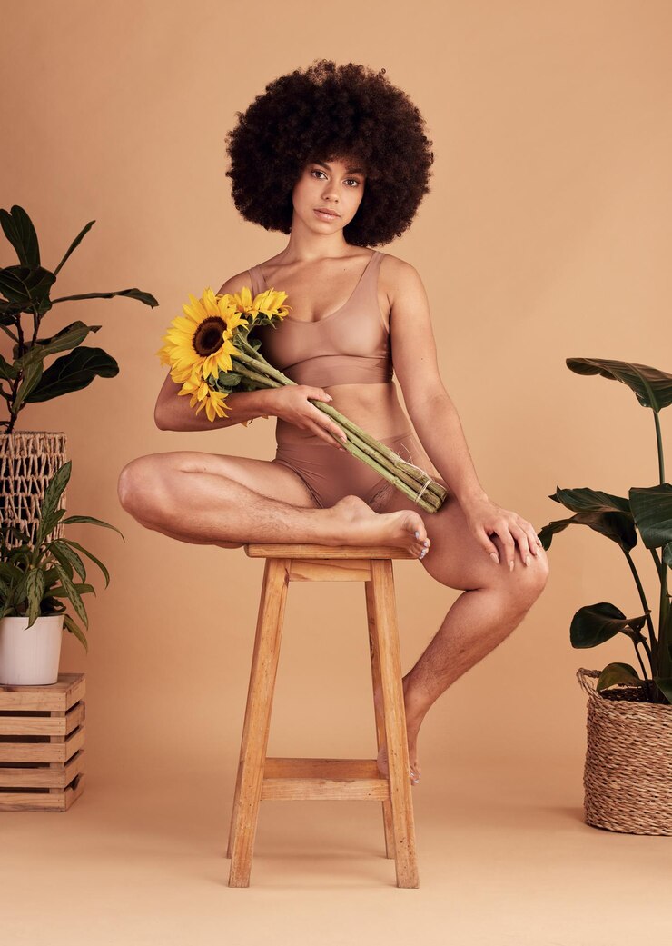 Foto flores de amor próprio e mulher negra em roupas íntimas para positividade corporal, empoderamento de beleza e forma corporal em um fundo de estúdio girassol criativo e retrato de uma modelo com confiança em sua pele