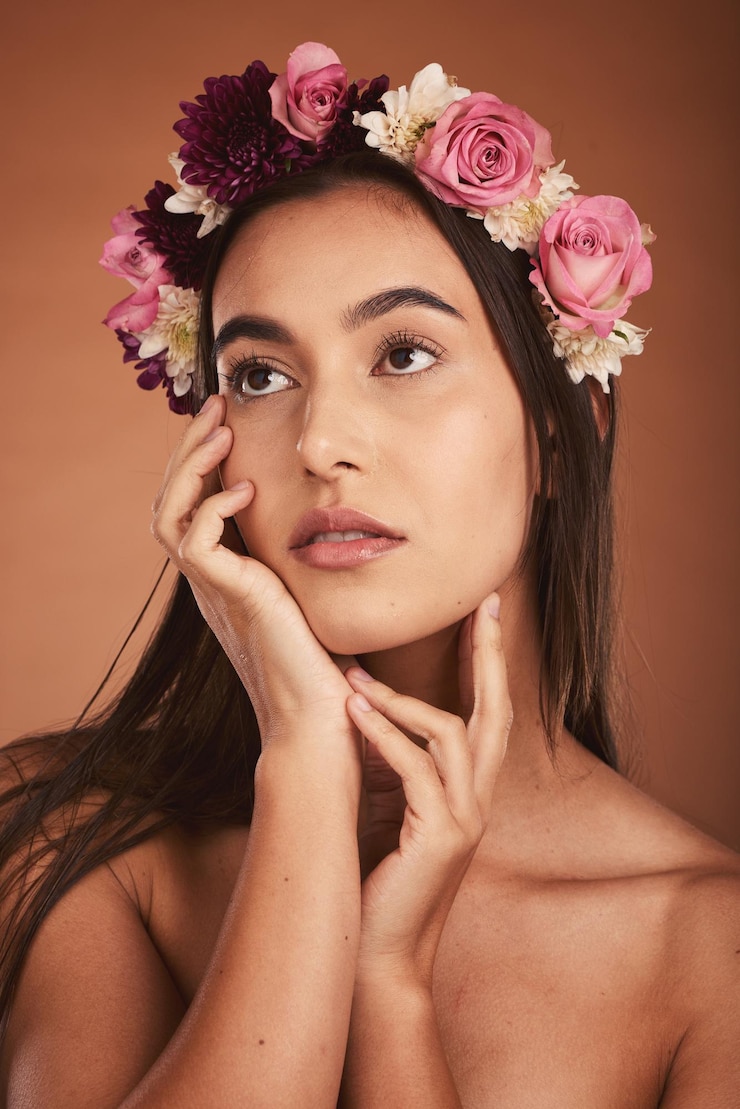 Foto flores de cabelo de beleza e mulher em maquiagem em fundo de estúdio marrom cosméticos florais cuidados com a pele e jovem modelo feminino elegante e pensativo posando com rosas ou plantas para tratamento de pele saudável