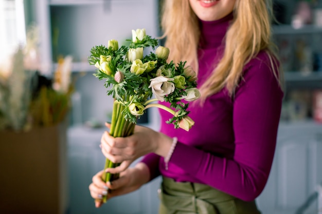 Flores de close-up na mão. Local de trabalho do florista. Mulher organizando um buquê com rosas, crisântemo, cravo e outras flores. Professora de floricultura em master classes ou cursos.