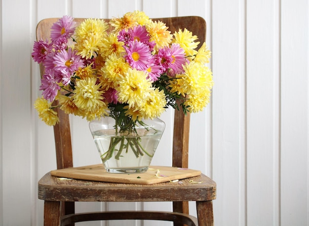 Flores de jardim de outono de crisântemos rosa e amarelo em um vaso de vidro em uma cadeira