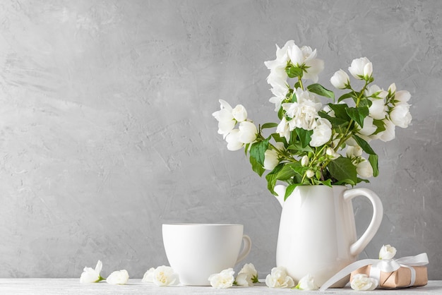 Flores de jasmim branco em um vaso com caixa de presente e xícara de café na mesa de madeira branca Natureza morta Fundo festivo