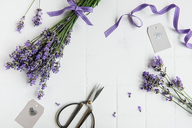 Flores de lavanda, tesoura e fita em um fundo de ladrilho branco