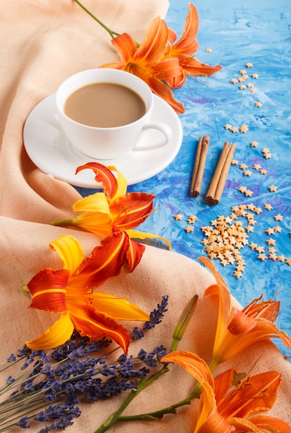 Flores de lírio-dia e lavanda laranja e uma xícara de café sobre um fundo azul de concreto