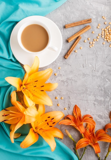 Flores de lírio-do-dia laranja e lavanda e uma xícara de café em um fundo cinza de concreto, com tecido azul. Morninig, primavera, composição da moda. Camada plana, vista superior, espaço de cópia.