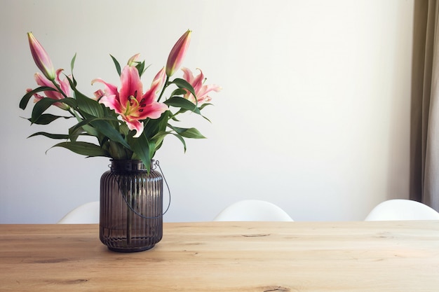 Flores de lírio rosa em um vaso em uma mesa de madeira no interior contra uma parede branca no quarto moderno