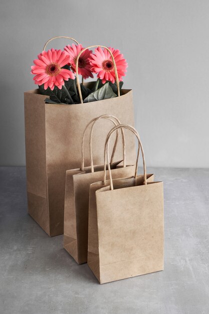 Flores de margarida gerbera coral e sacolas de papel artesanal na parede de papel verde, texto "Venda de primavera"