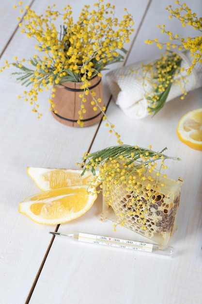 Flores de mimosa, favo de mel, dois pedaços de limão em uma superfície de madeira de cor leite.