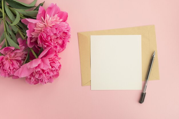 Flores de peônia rosa e envelope com cartão em branco na mesa