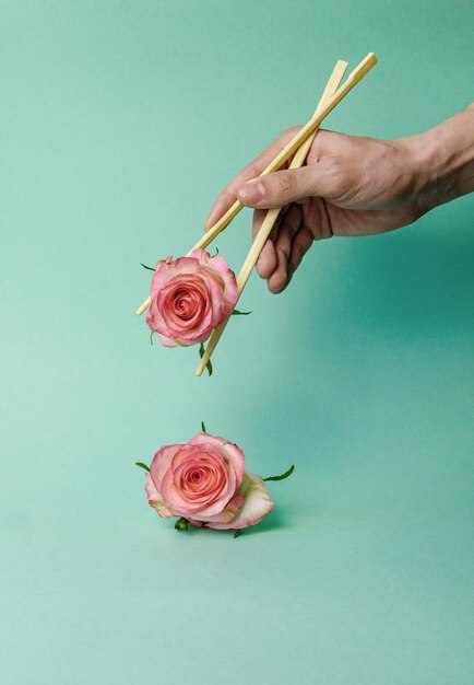 Foto flores de rosa em mãos jovens com pauzinhos em cores pastel um conceito minimalista da natureza