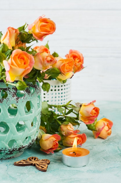 Flores de rosas laranja frescas em vaso de hortelã e vela acesa