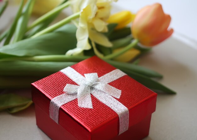 Flores de tulipa amarela com caixa de presente vermelha em cima da mesa.