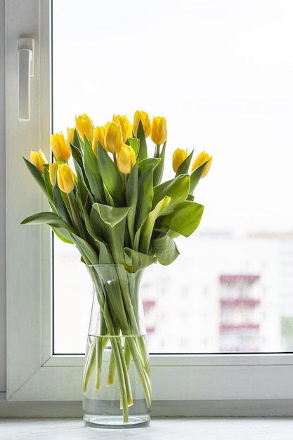 Flores de tulipa amarela em vaso de vidro no peitoril da janela