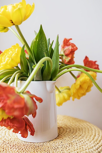 Flores de tulipa florescendo vermelho amarelo desfocado com caules verdes e folhas em jarro de cerâmica branca sobre fundo de parede branca clara Papel de parede de botânica floral criativo Cartão de saudação criativo mínimo