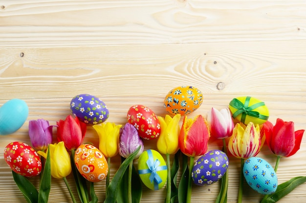 Flores de tulipas coloridas e ovos de páscoa no fundo da mesa de madeira com espaço para texto