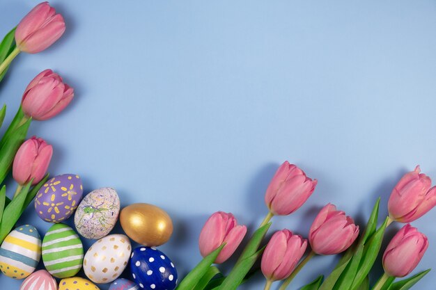 Flores de tulipas cor de rosa e ovos coloridos isolados em azul