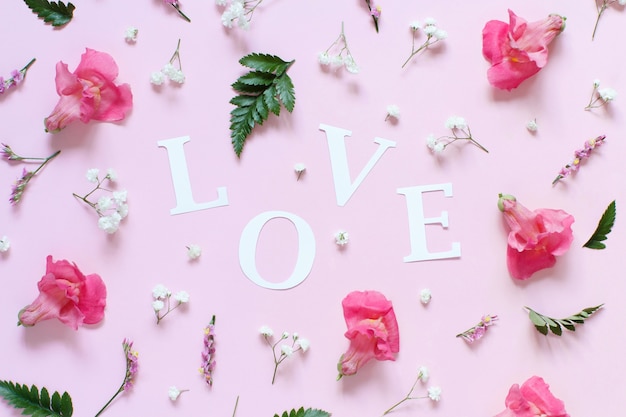 Flores e a palavra Amor em uma vista superior de fundo rosa claro